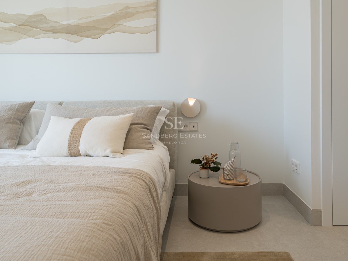 Close-up of a bed with beige linen bedding next to a round minimalist nightstand and abstract wall art.