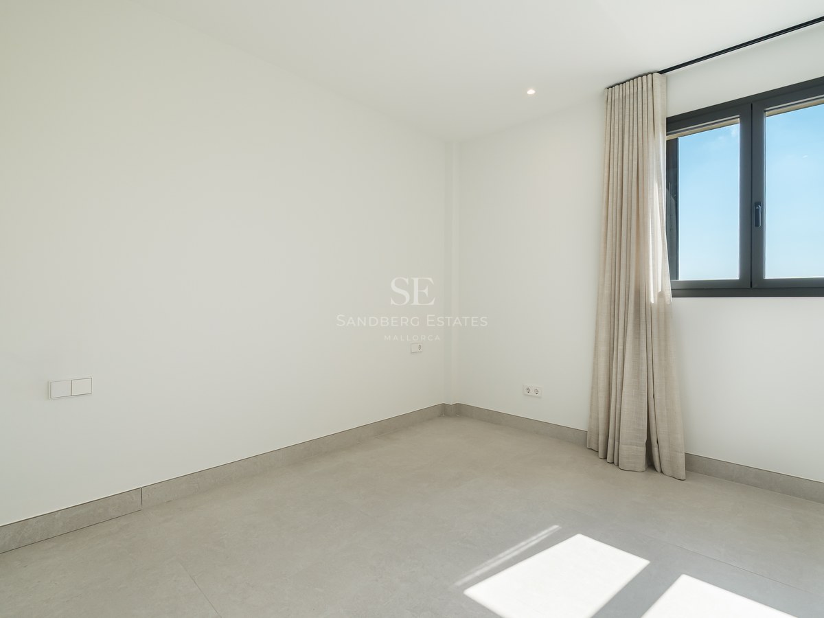 An empty minimalist room with white walls, large gray floor tiles, and a window with neutral curtains.