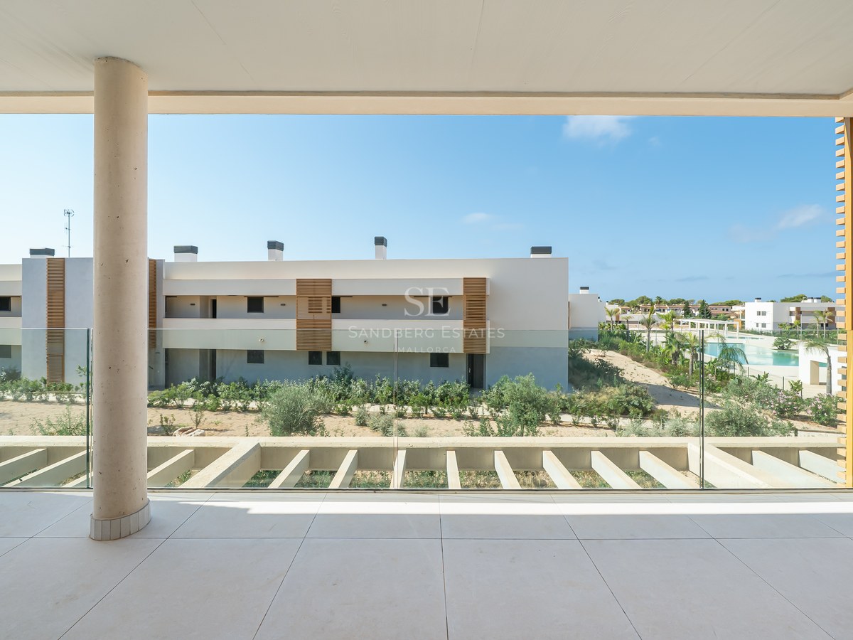 A spacious covered terrace with glass balustrades and concrete pillars overlooking modern apartments and a pool.