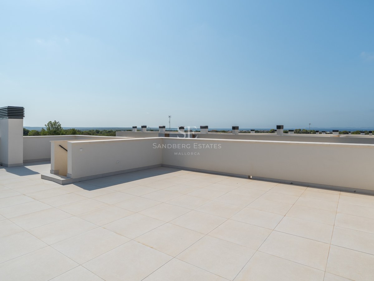 Large rooftop terrace with cream porcelain tiles and white plastered walls under a clear blue sky with sea views.