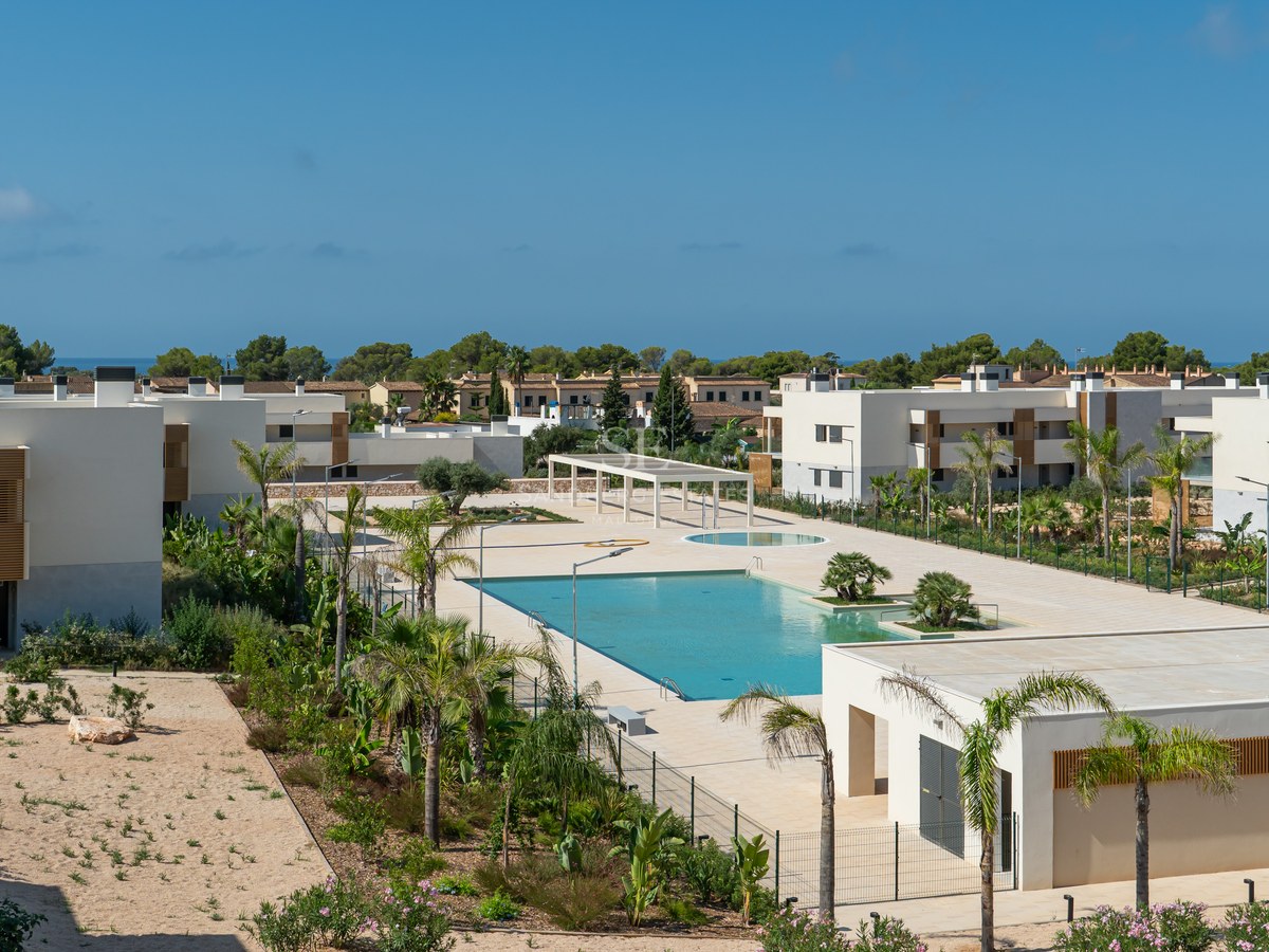 Elevated view of a large turquoise swimming pool within a modern residential complex with white buildings and palms.