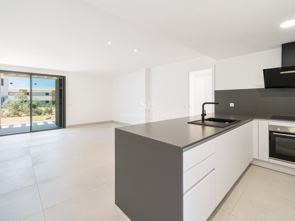 Minimalist white kitchen featuring a grey island, black appliances, and large sliding glass doors leading outside.