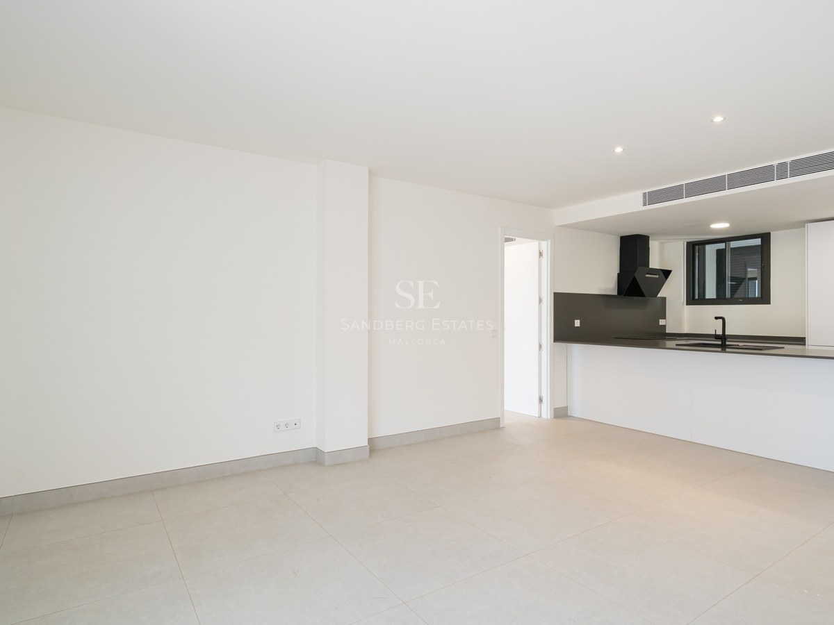 Clean minimalist kitchen with white cabinetry, dark countertops, and large grey floor tiles in an open living space.