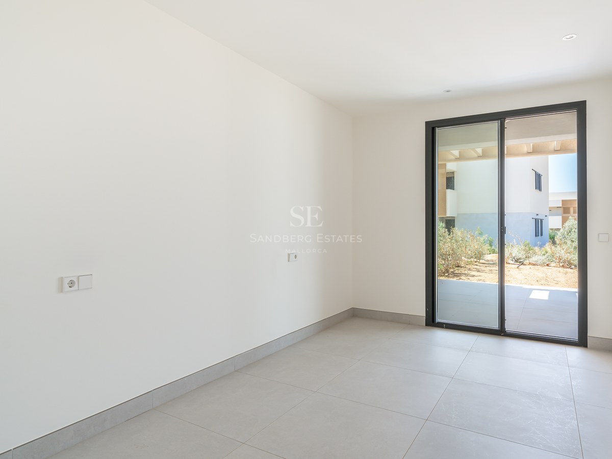 Empty modern bedroom with white walls, grey tile flooring, and sliding glass door opening to a private garden patio.