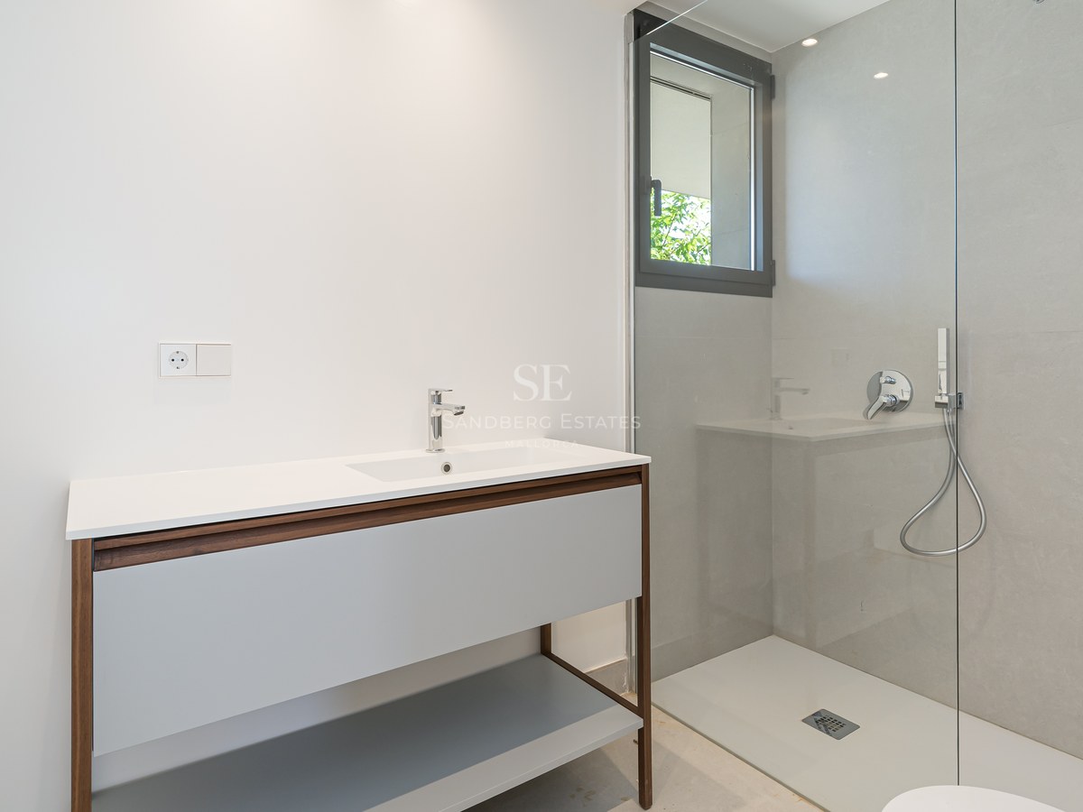 Modern bathroom featuring a wood-framed vanity, glass shower partition, and large-format grey wall tiles.