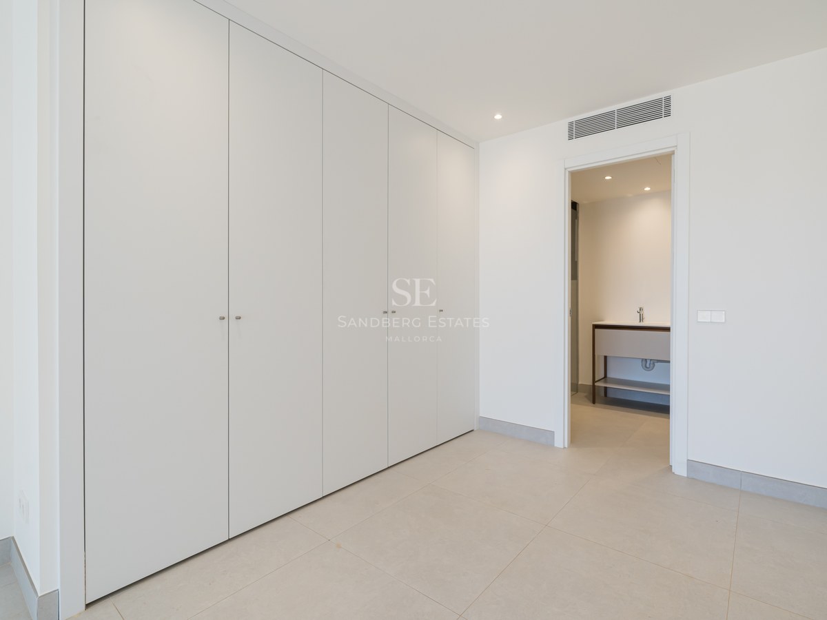 Minimalist white floor-to-ceiling built-in wardrobes in a bright room with an open door to a modern bathroom.