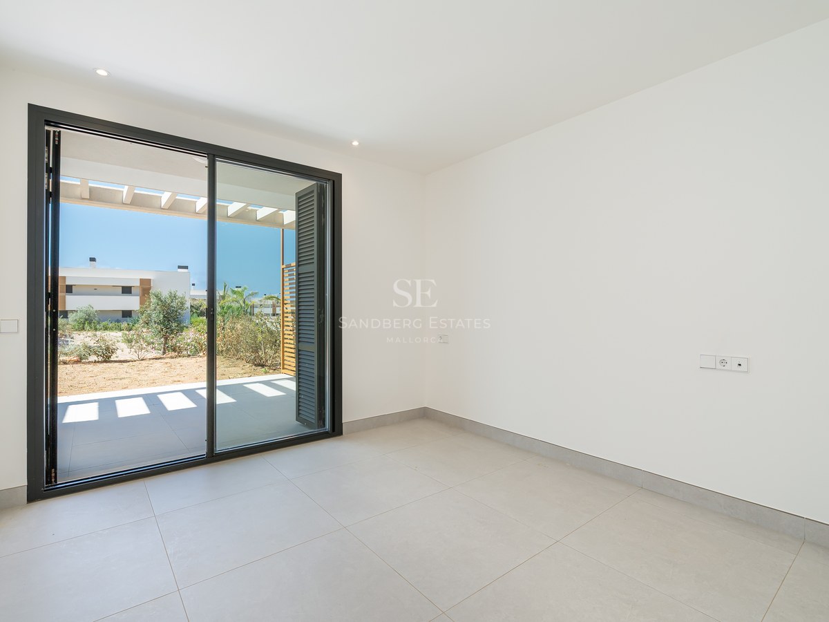 Empty modern room with white walls, grey tiled flooring, and a large sliding glass door opening onto a sunlit terrace.