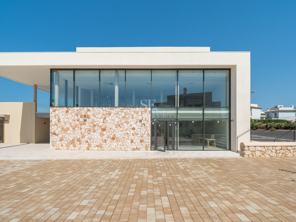 Modern building facade featuring large glass windows, a natural stone feature wall, and an expansive paved courtyard.