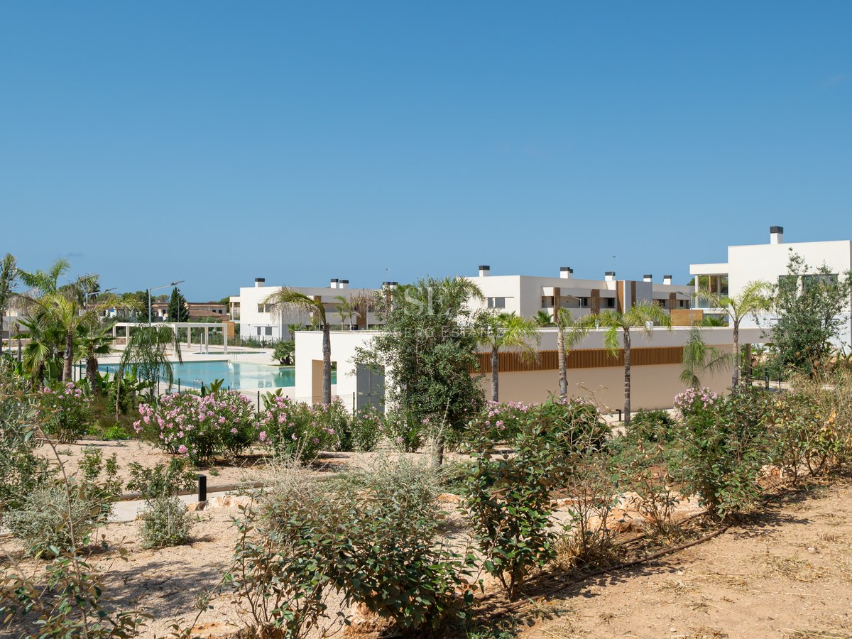 Contemporary white apartment buildings with a large swimming pool surrounded by palm trees and Mediterranean gardens.