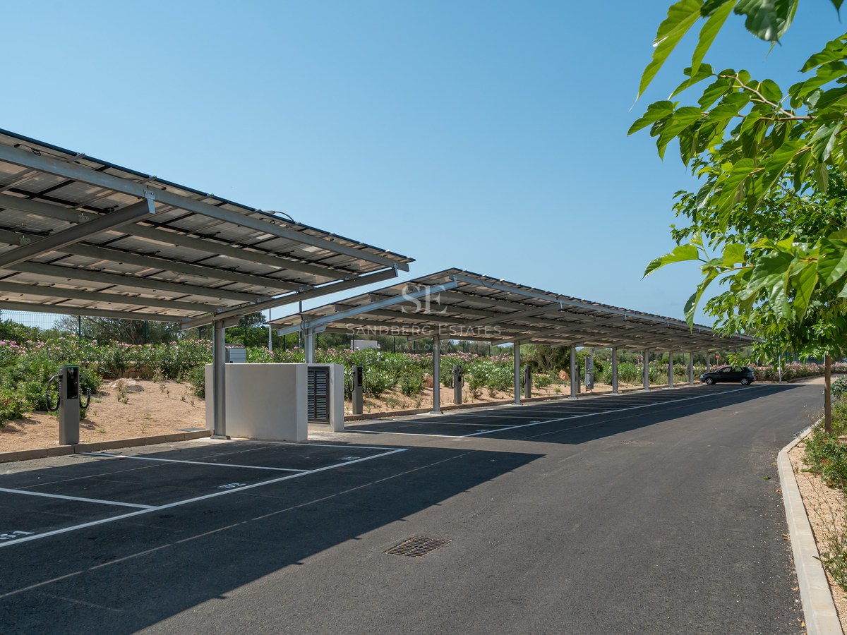Modern outdoor parking area featuring solar panel roof structures and electric vehicle charging stations under a clear sky.