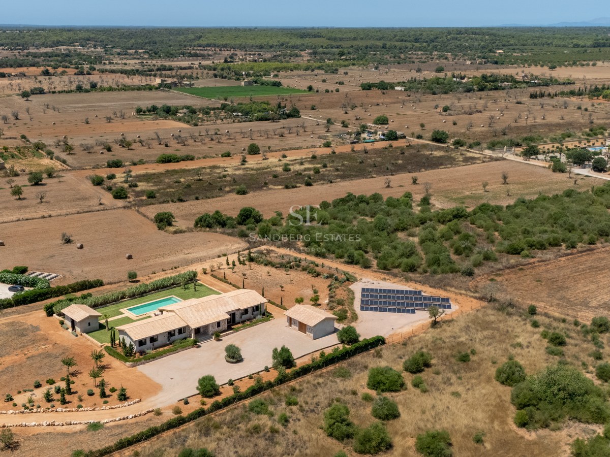 Vue aérienne d'une villa de luxe avec piscine et panneaux solaires dans un vaste paysage rural préservé.