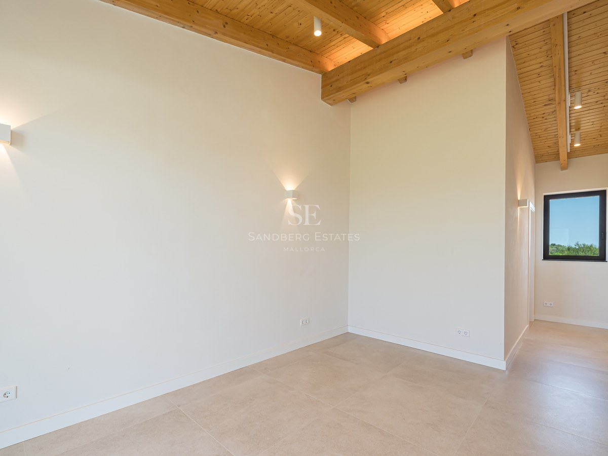 Chambre épurée avec plafond voûté en bois, sol en grès cérame beige et murs blancs avec appliques murales.