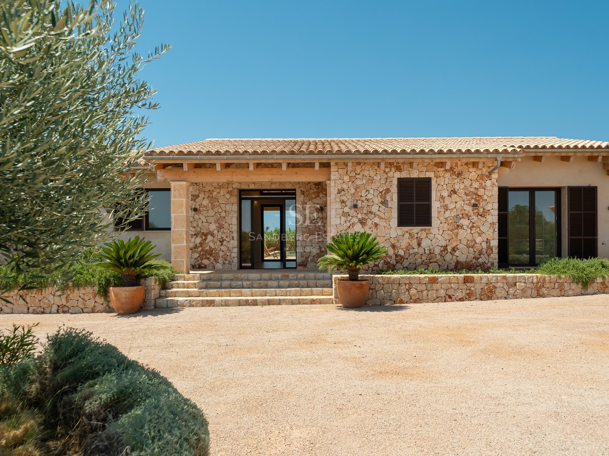 Entrée de villa de luxe avec murs en pierre naturelle, toit en terre cuite et allée en gravier.