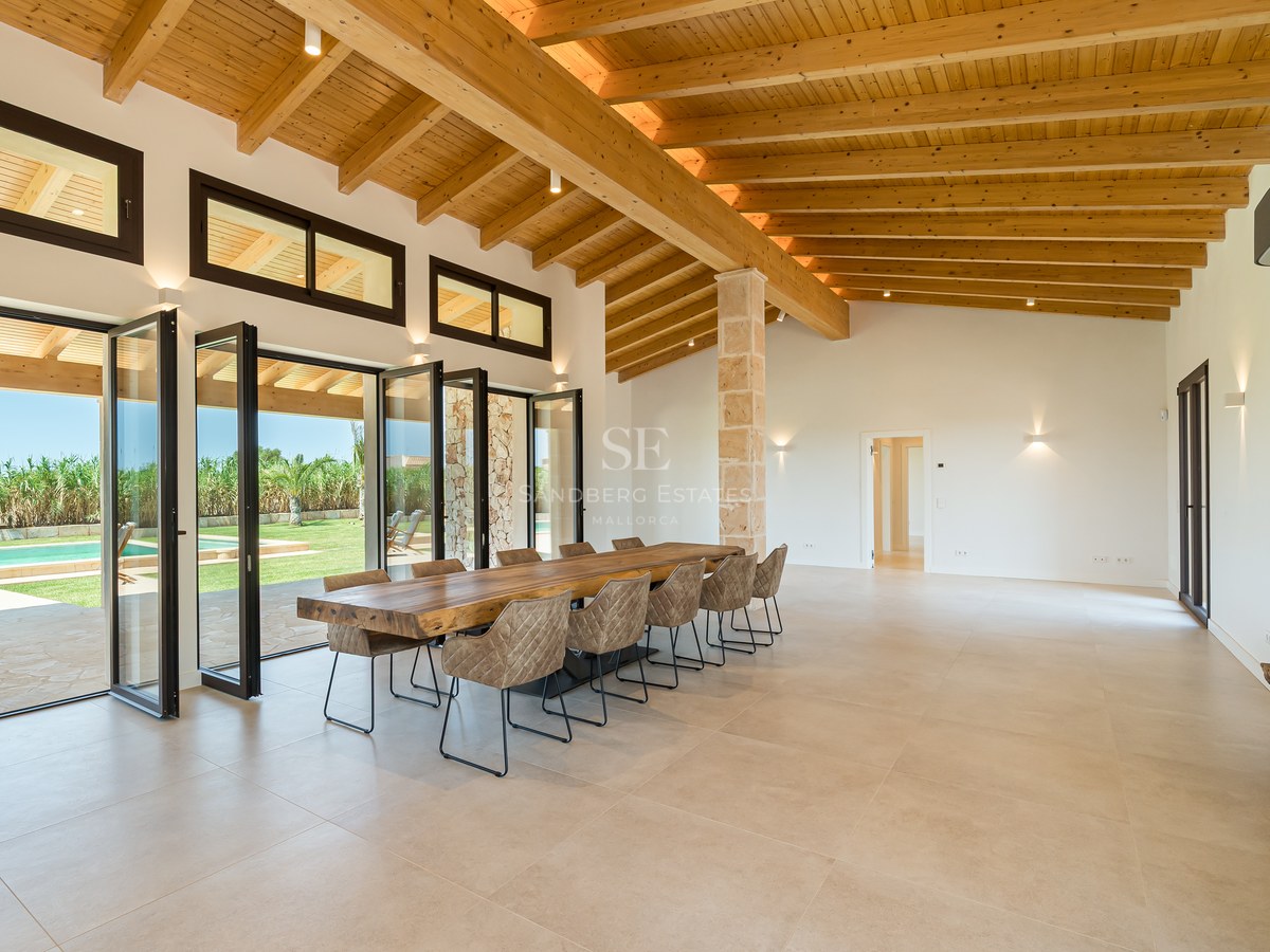 Grande salle à manger avec hauts plafonds en bois et baies vitrées pliantes ouvrant sur le jardin et la piscine.