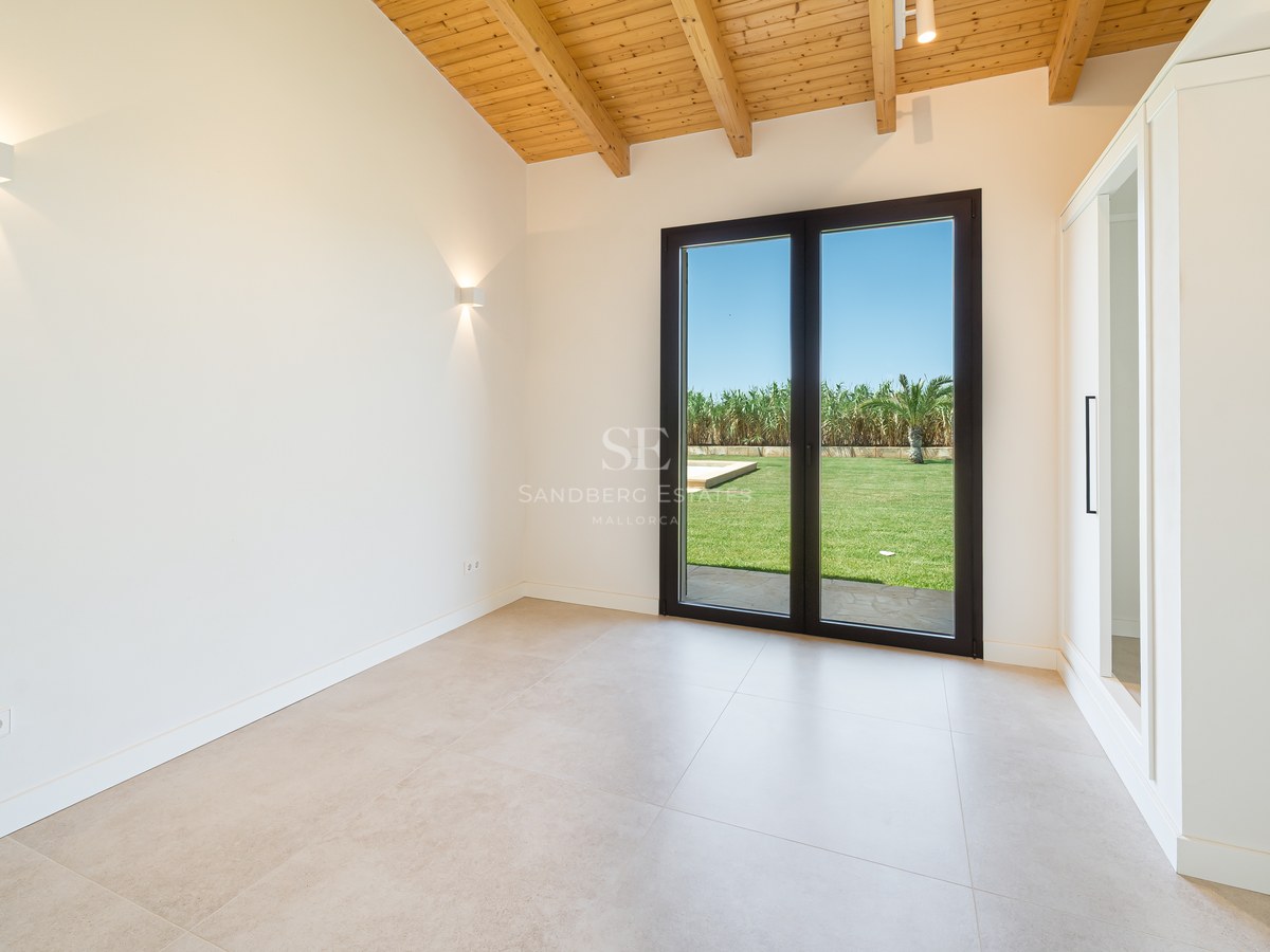 Chambre vide avec plafond voûté en bois, grandes baies vitrées ouvrant sur le jardin et placards blancs.