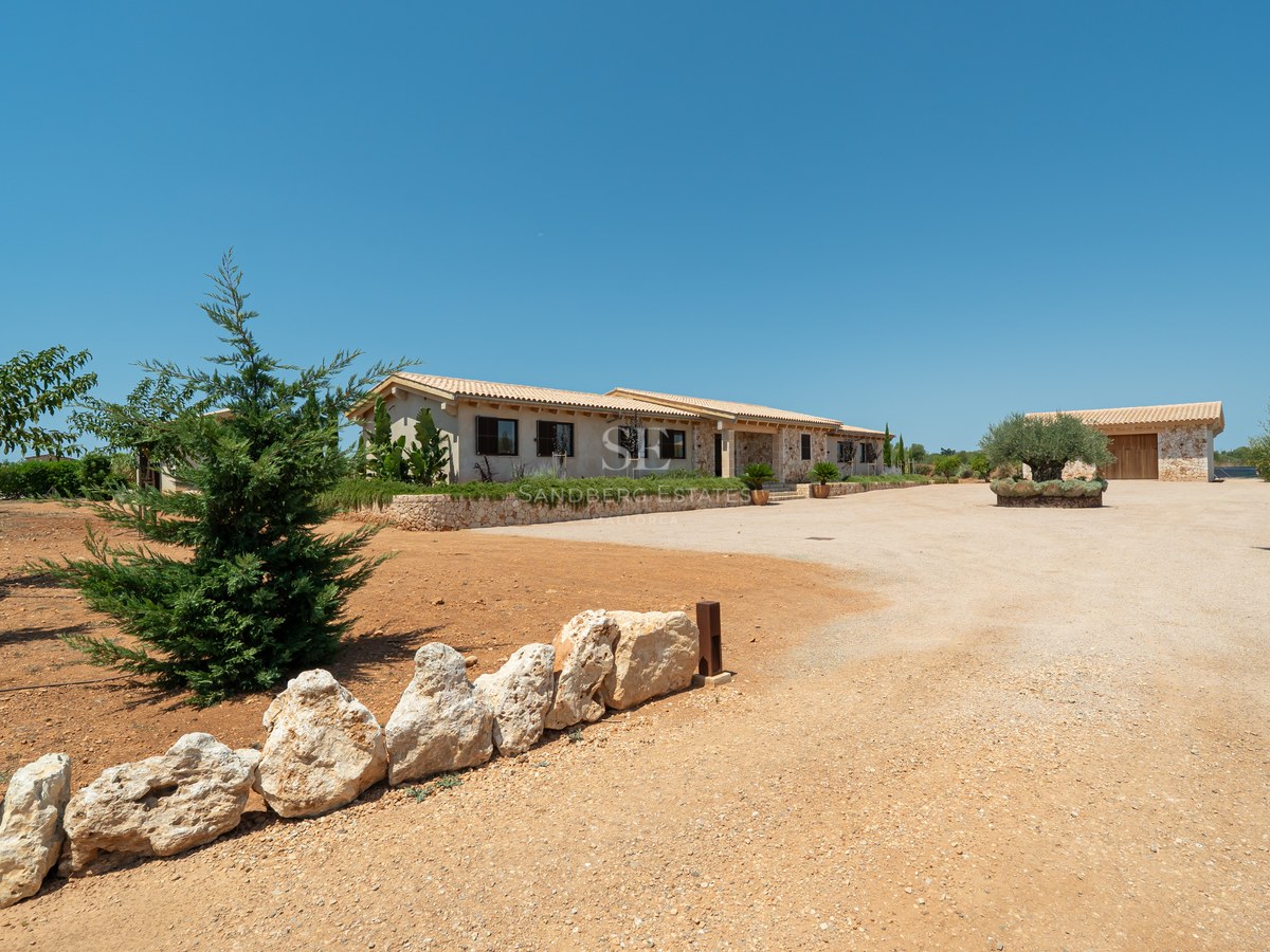 Façade d'une villa méditerranéenne avec murs en pierre, toit en terre cuite et allée de gravier sous un ciel bleu.