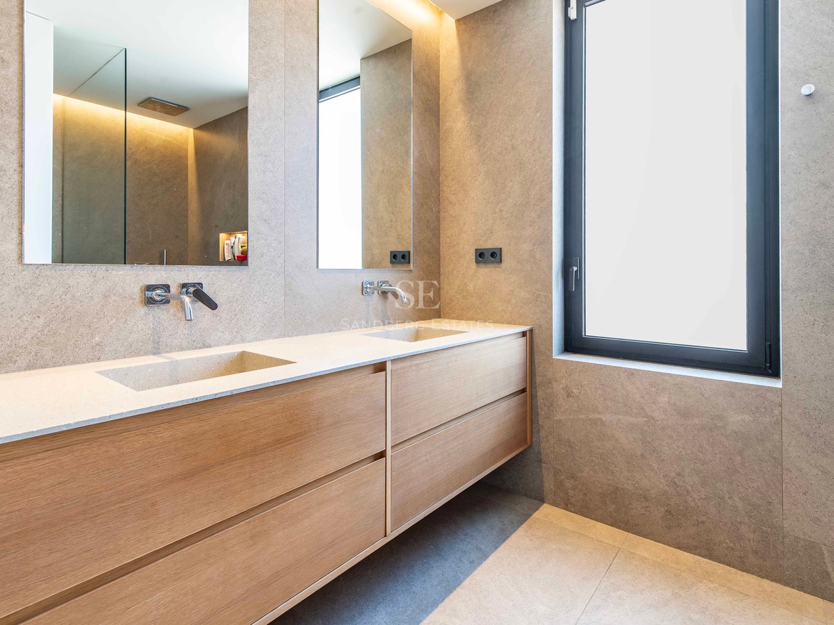 Luxury bathroom featuring a double wood vanity with integrated stone sinks and large mirrors against stone walls.