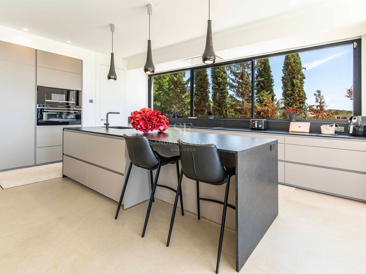 Modern minimalist kitchen featuring a charcoal stone island, handleless grey cabinets, and a wide panoramic window.