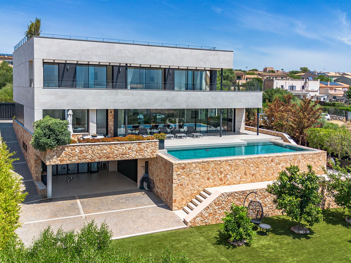 Three-story modern villa featuring a turquoise infinity pool, natural dry-stone walls, and expansive glass balconies.