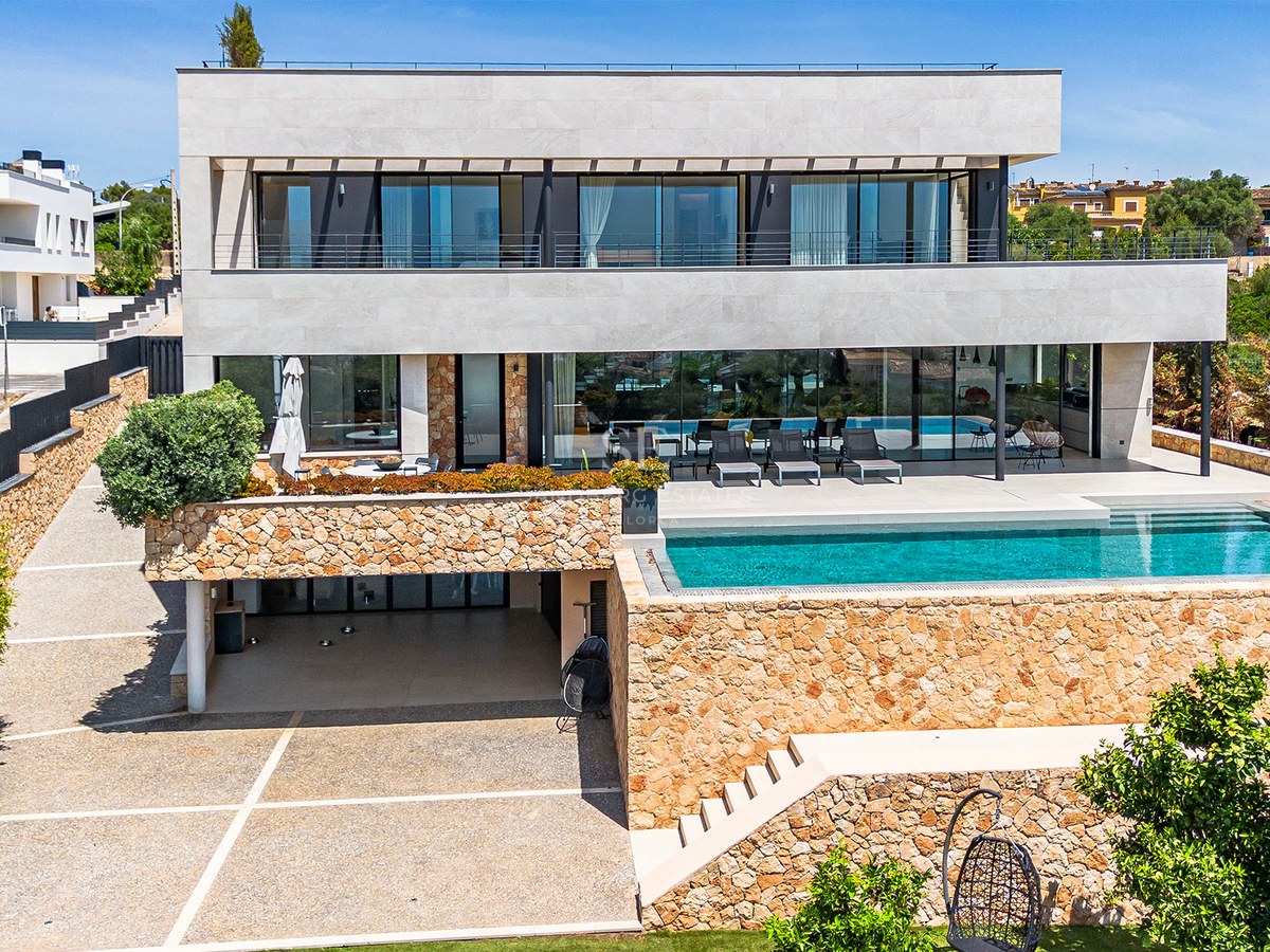 Exterior view of a three-story contemporary villa featuring natural stone walls, large glass windows, and a turquoise pool.
