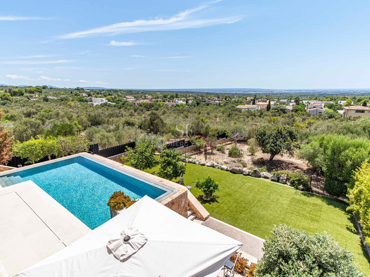 Elevated view of a rectangular blue swimming pool surrounded by a natural stone terrace and lawn overlooking the sea.