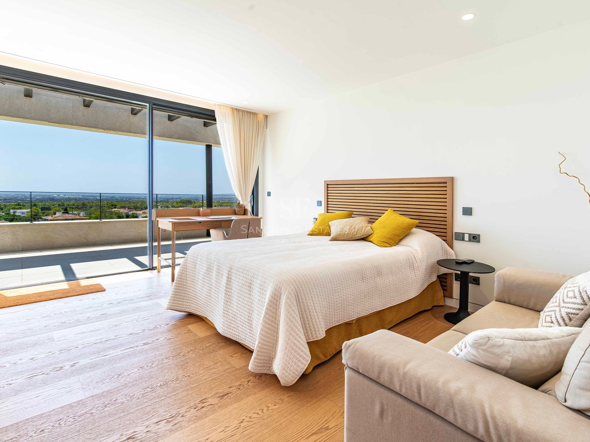 Modern master bedroom featuring oak floors, a double bed, integrated desk, and large glass doors opening to a terrace.