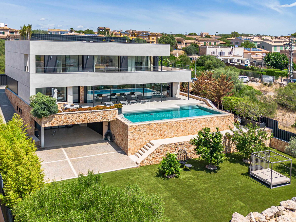 Elevated view of a three-story contemporary villa with stone walls, glass balconies, swimming pool, and green lawn.