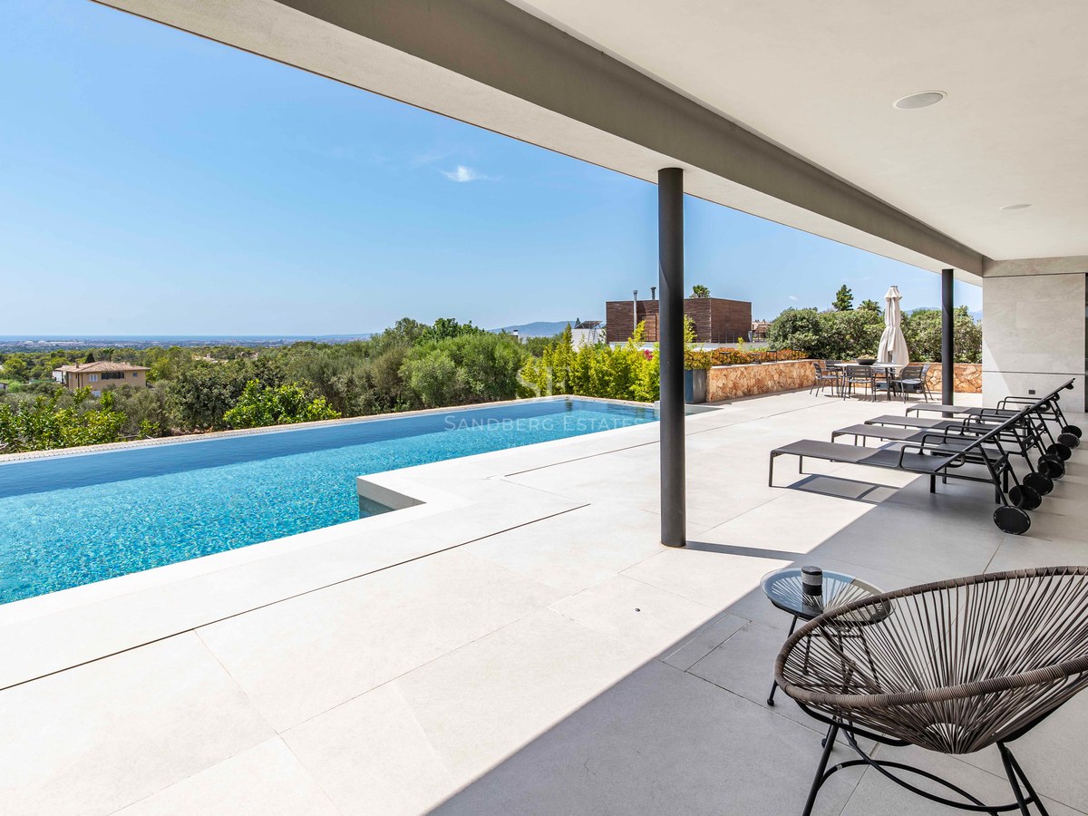 Infinity pool on a white stone terrace with black loungers and panoramic views of the green valley and sea.