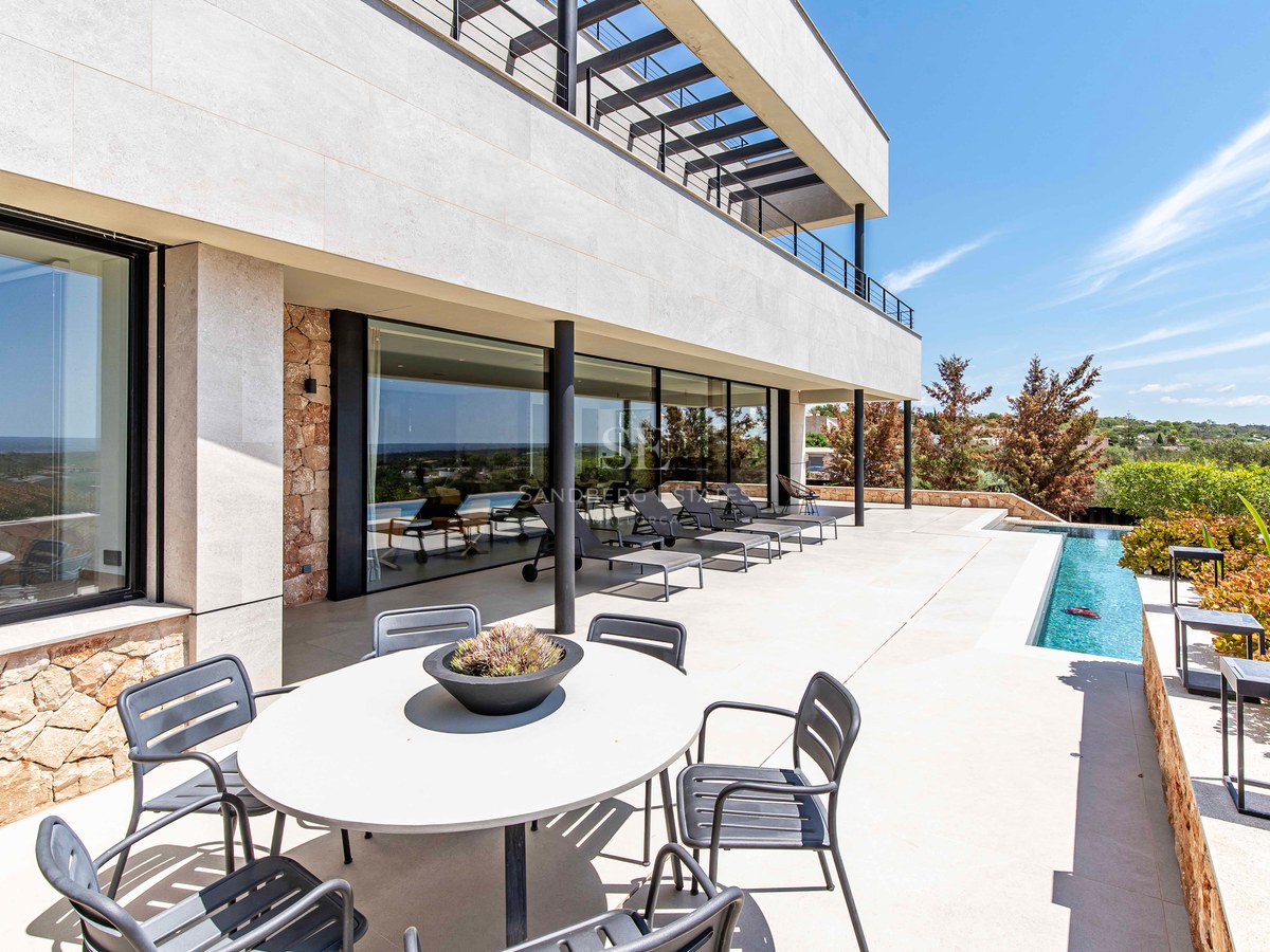 Sun-drenched terrace with grey loungers, outdoor dining area, and a sleek pool against a modern stone facade.