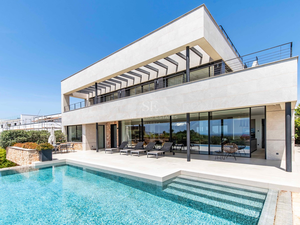 Luxury villa facade featuring a crystal-blue swimming pool, expansive glass windows, and stone cladding under a clear sky.