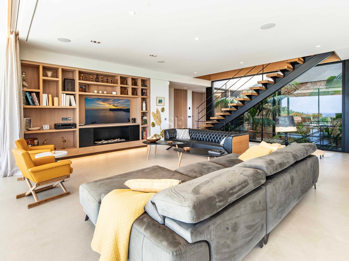 Modern living room featuring a grey sectional sofa, custom oak shelving, and a floating staircase with garden views.