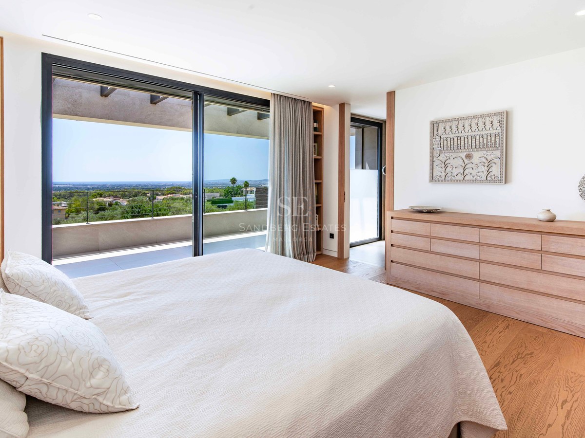 Modern bedroom featuring oak floors, light wood furniture, and glass doors opening to a terrace with sea views.