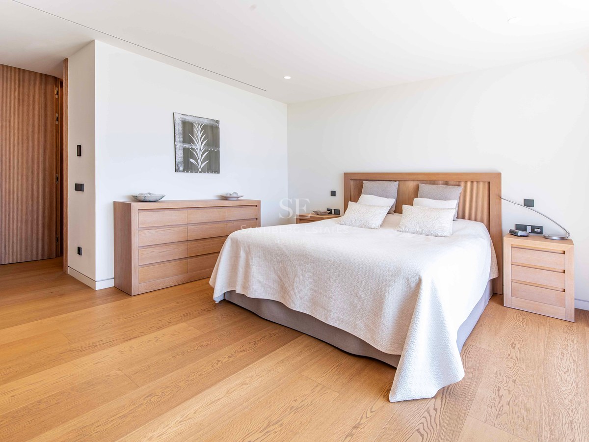 Bright modern bedroom featuring light oak flooring, a matching wood headboard, and minimalist white walls.