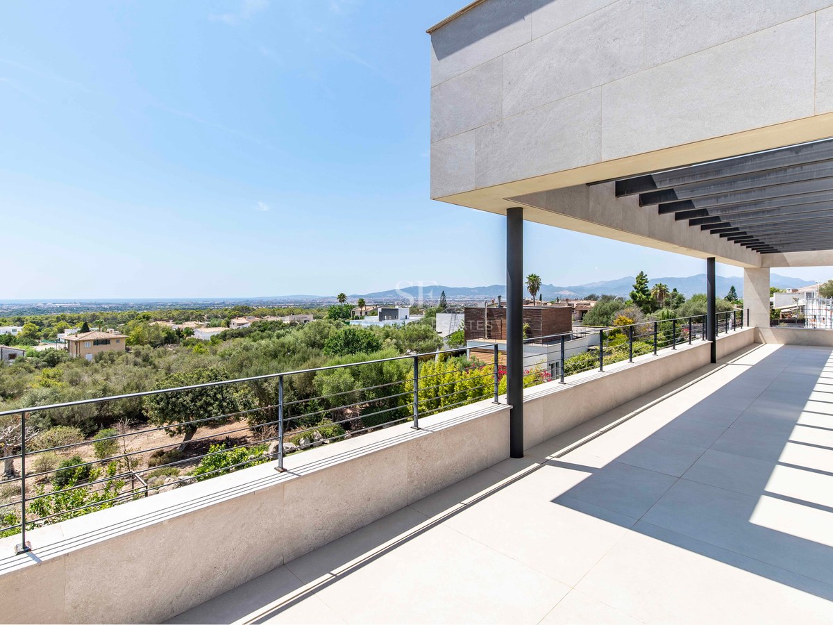 Large modern terrace with stone tiling and metal railings overlooking a green valley towards the Mediterranean sea.