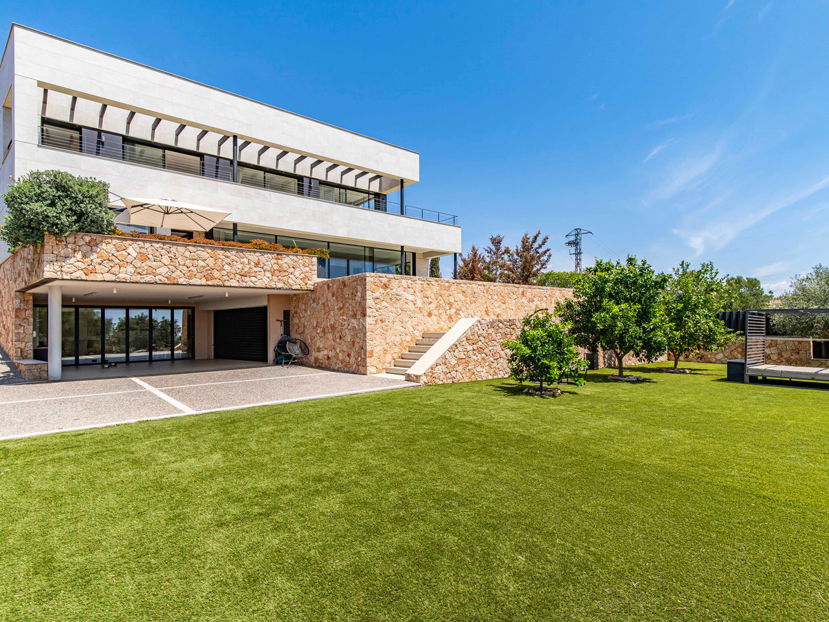 Modern white villa with natural stone walls, a large green lawn, and minimalist landscaping under a clear blue sky.