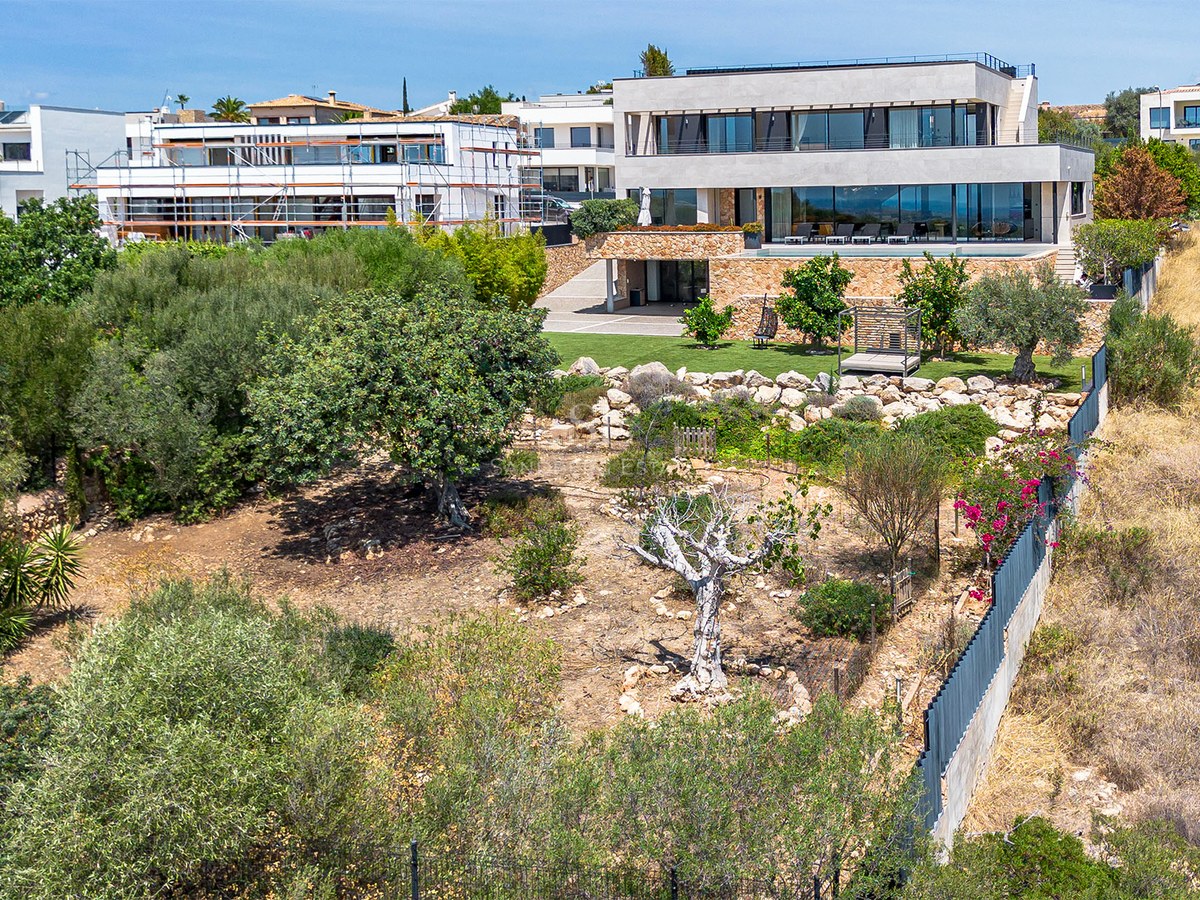 Side view of contemporary villa with tiered gardens and natural stone walls against a blue sky.