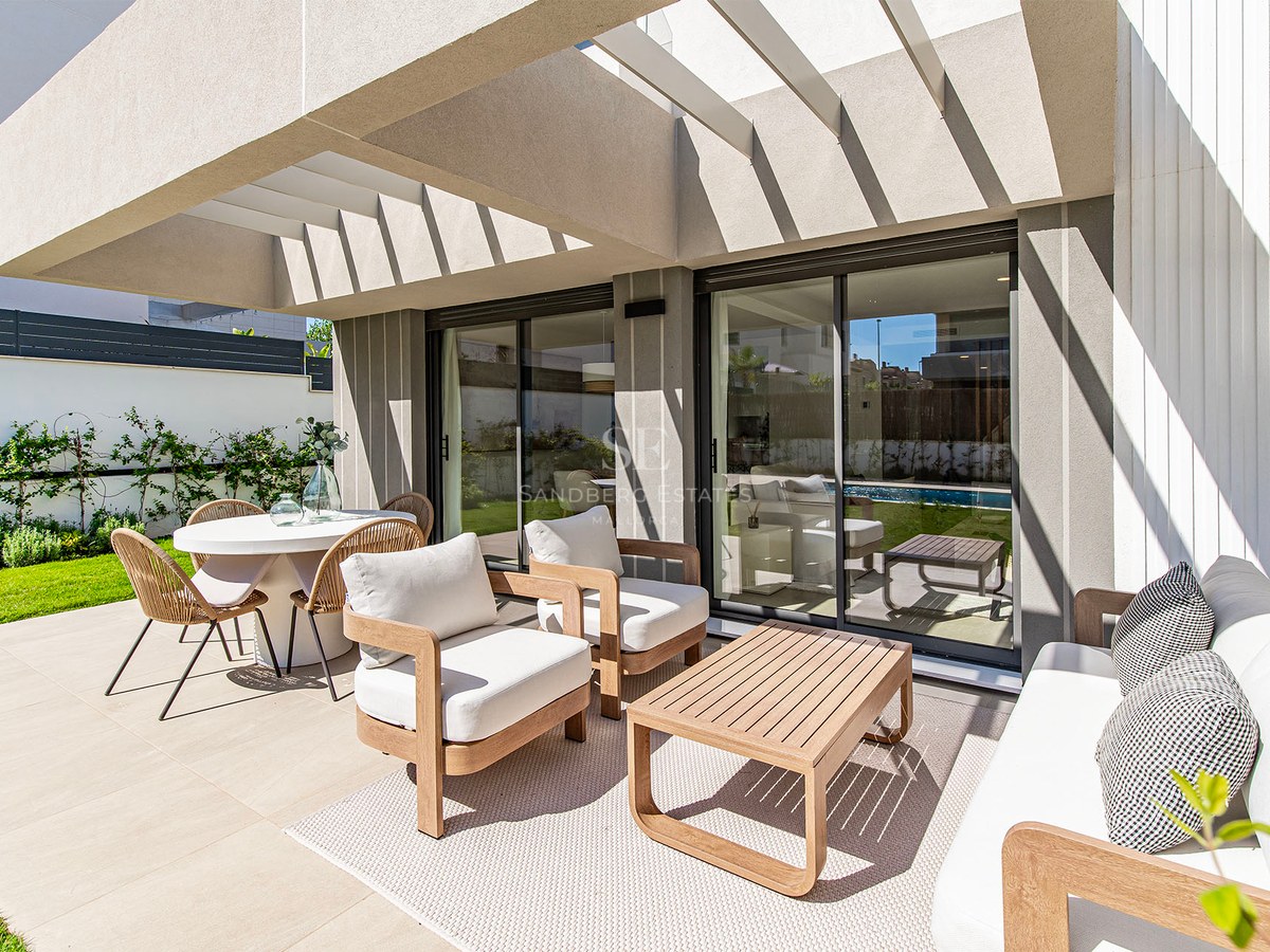 Terraza contemporánea con comedor exterior blanco, muebles de salón en madera y pérgola junto al jardín.