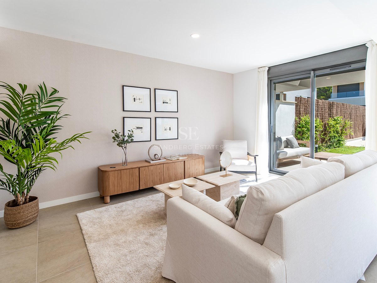 Salón contemporáneo con sofá crema, aparador de madera y puertas correderas de cristal hacia el jardín.