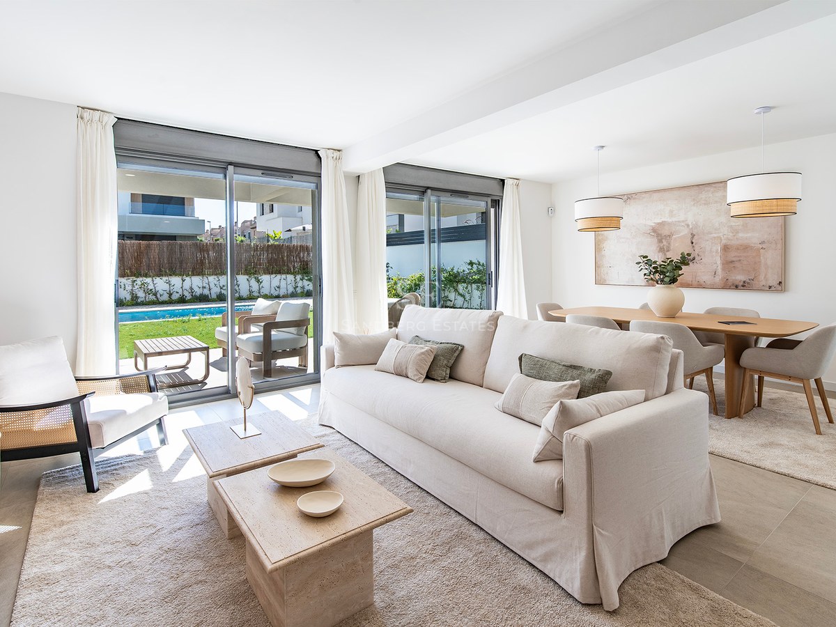 Salón moderno con sofá crema, mesas de piedra y ventanales con vistas a la piscina y el jardín privado.