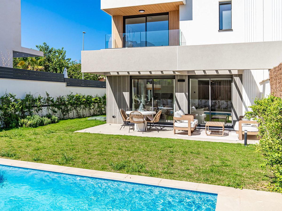 Villa contemporánea con piscina turquesa, césped cuidado y terraza sombreada con mobiliario de diseño.