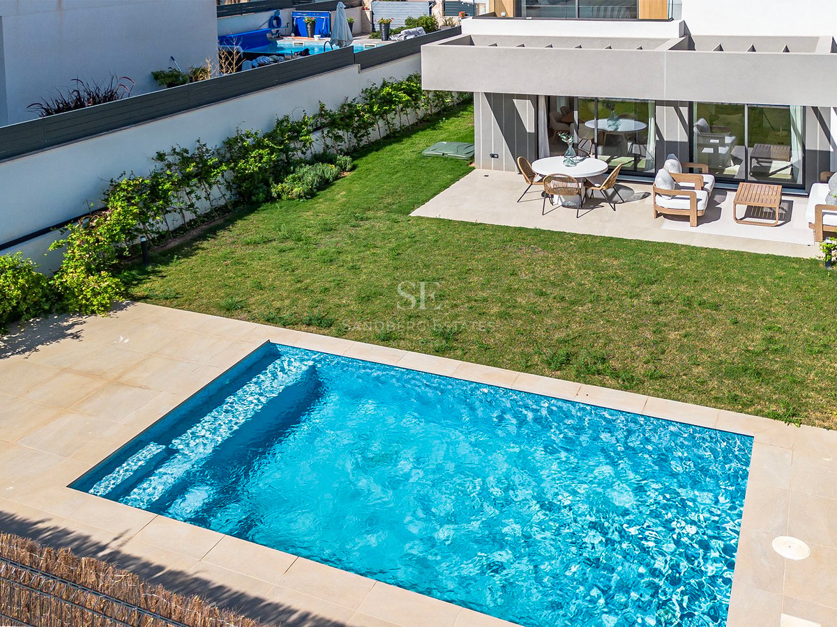Draufsicht auf einen rechteckigen blauen Pool, Rasenfläche und eine moderne Terrasse mit weißen Gartenmöbeln.