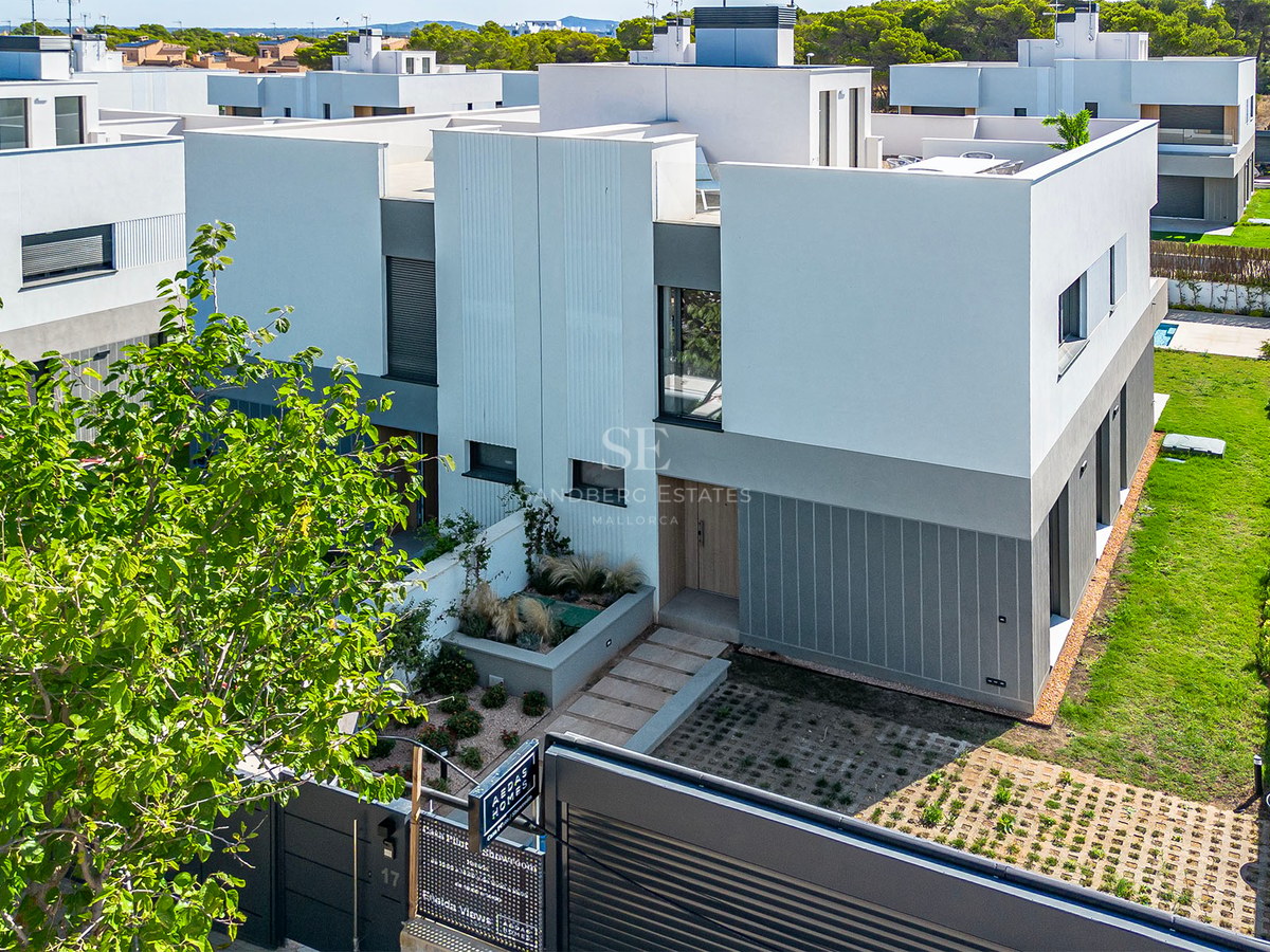 Außenansicht einer modernen weiß-grauen Villa mit Dachterrasse und gepflegtem Eingangsbereich bei Tageslicht.