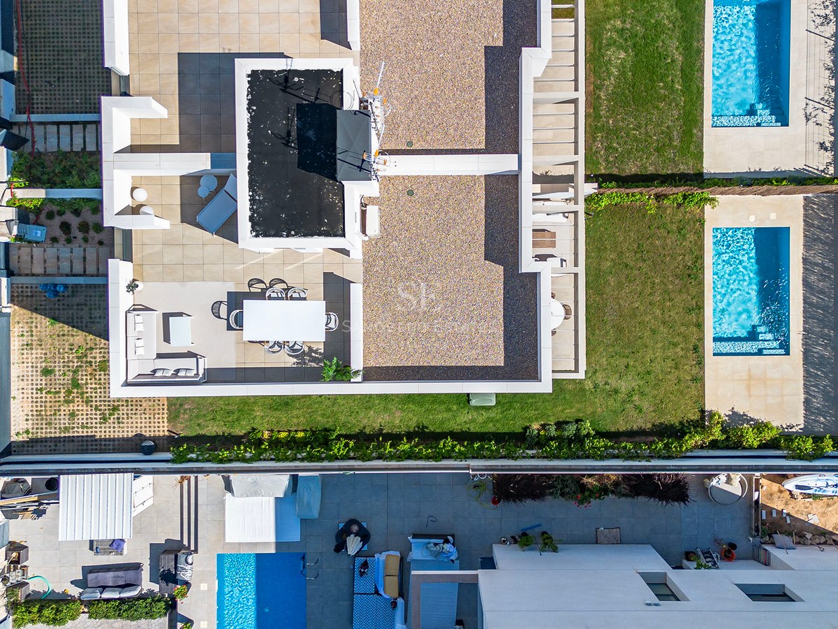 Draufsicht einer modernen Villa mit weißen Terrassen, Rasenflächen und zwei türkisfarbenen Pools.
