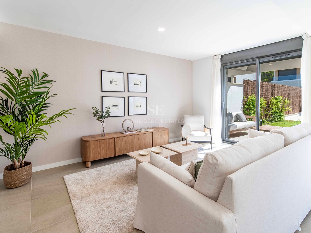 Helles Wohnzimmer mit cremefarbenem Sofa, Holz-Sideboard und Glasschiebetüren zu einer sonnigen Gartenterrasse.