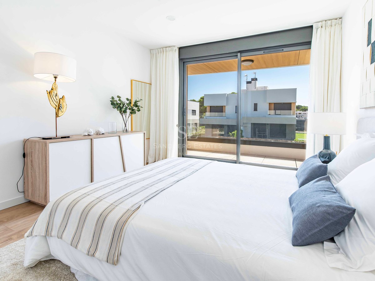 Modernes Schlafzimmer mit weißem Bett, blauen Kissen, Holzboden und großen Glastüren zur Terrasse.