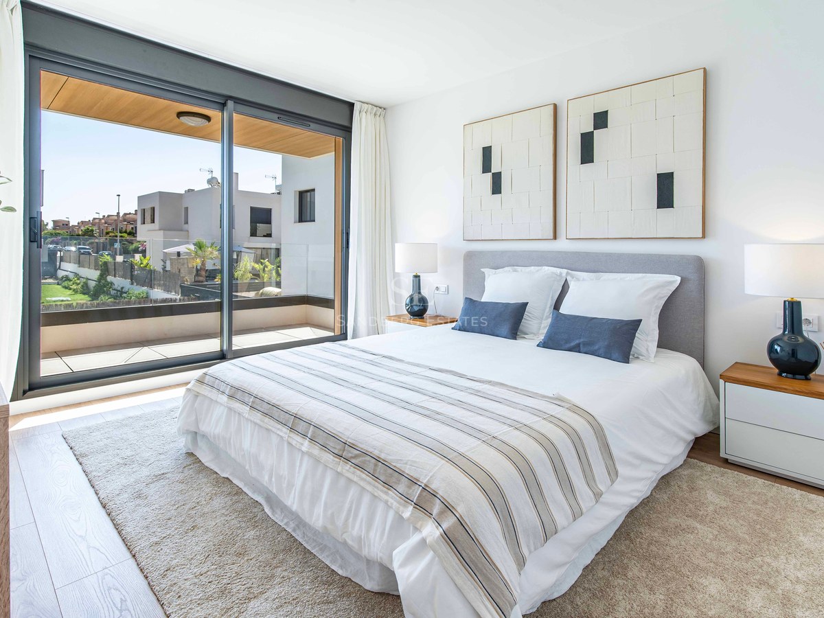 Helles, modernes Hauptschlafzimmer mit großem Doppelbett, neutralen Tönen und Glasschiebetüren zur Terrasse.