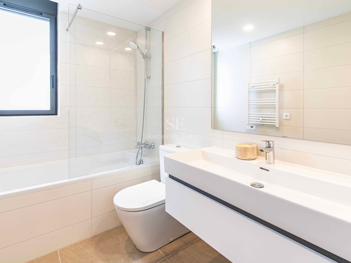 Zeitgenössisches Badezimmer mit Badewanne, Glasduschwand, Hänge-WC und breitem weißem Waschtisch.