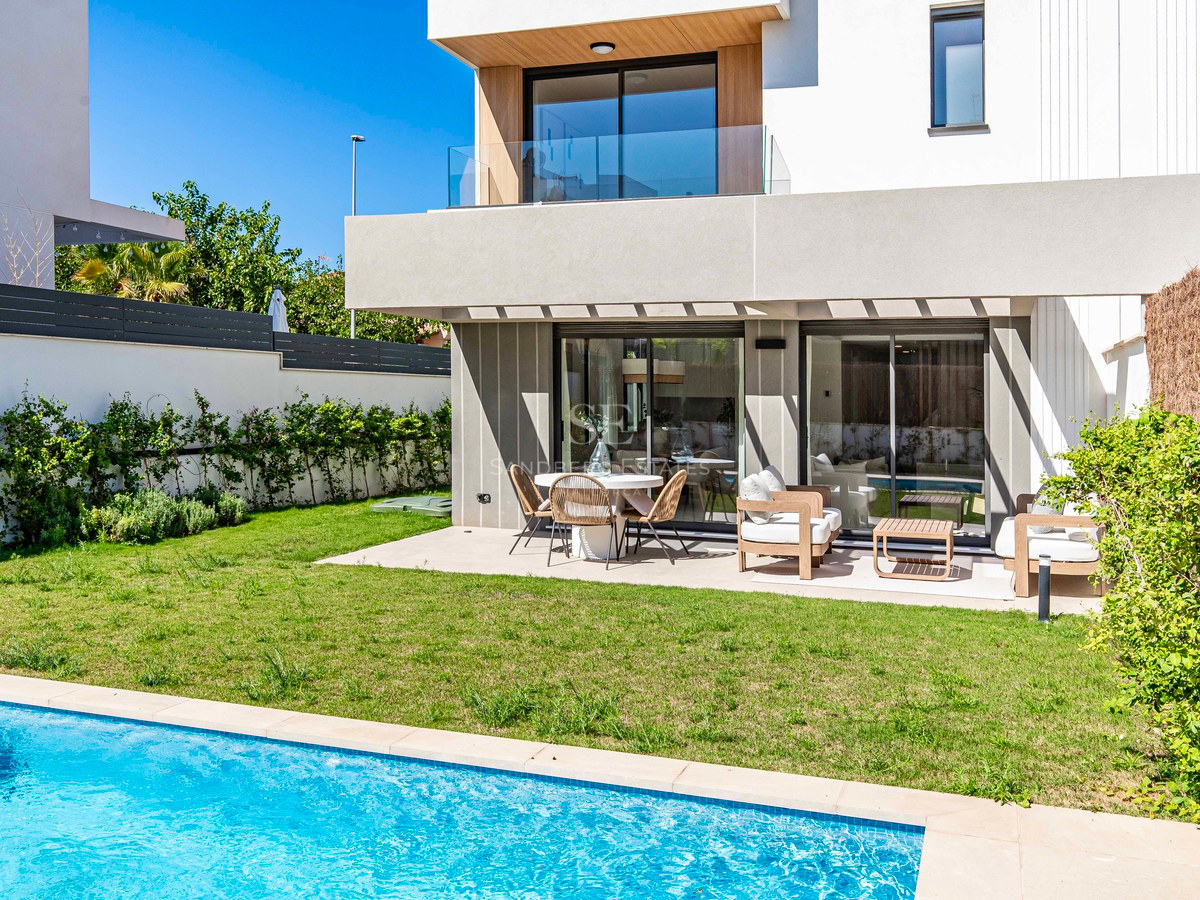 Moderne weiße Villa mit türkisfarbenem Pool, grünem Rasen und möblierter Terrasse unter blauem Himmel.