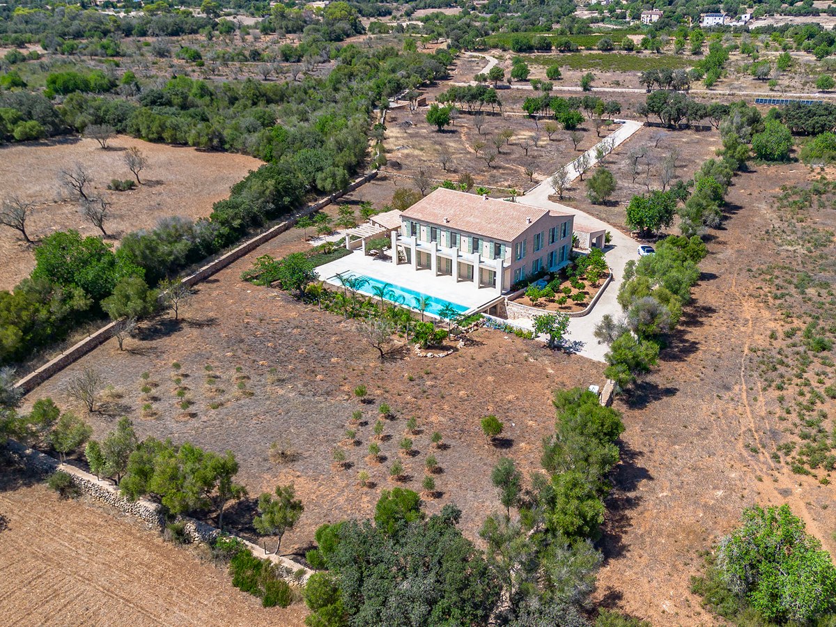 Vista aérea de una gran villa de dos plantas con piscina alargada, situada en una extensa finca rural con árboles.