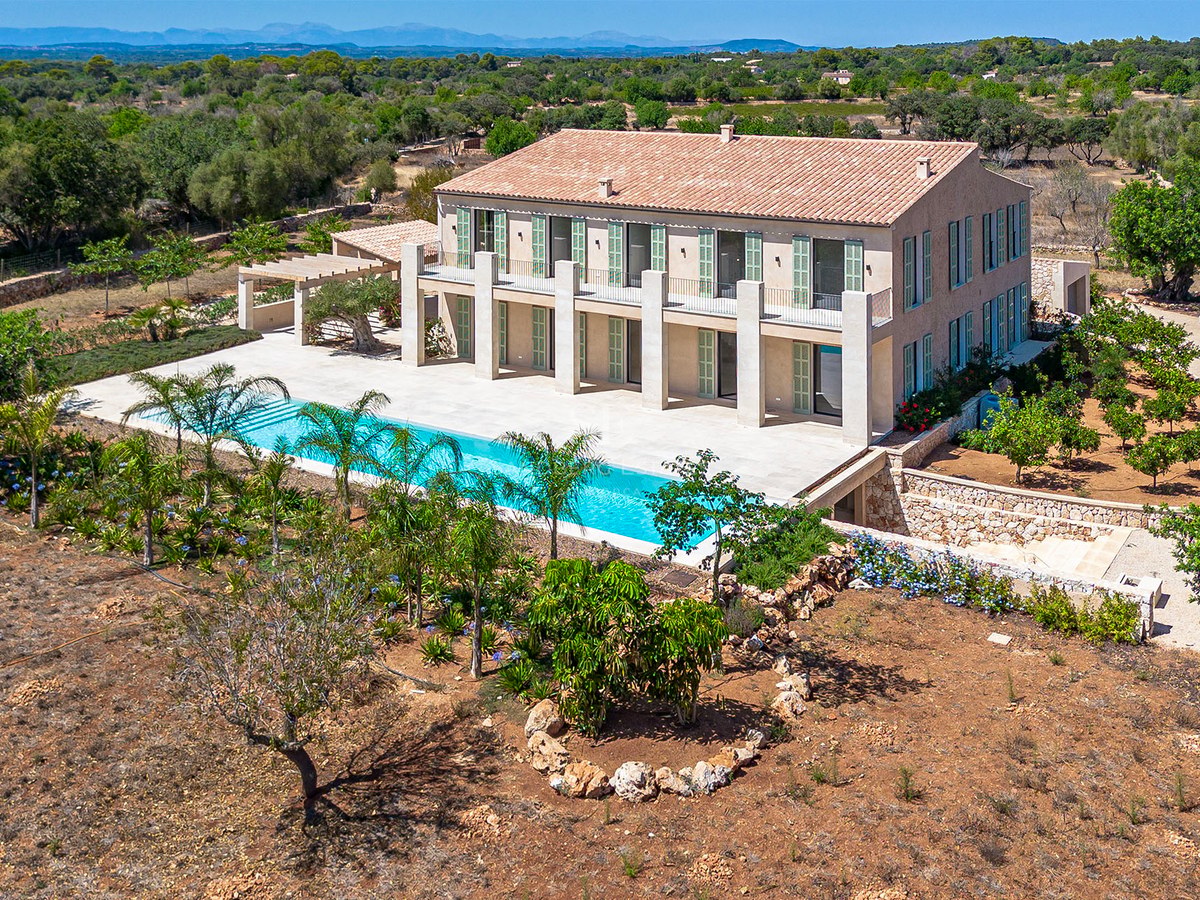 Vista aérea de una gran villa de piedra de dos plantas con piscina alargada y jardines en un entorno rural.